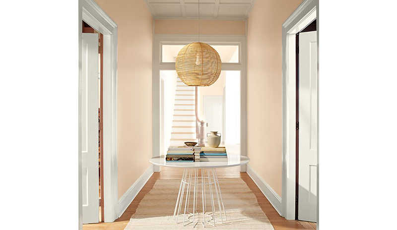 A peach-painted hallway with white doors and trim, rattan ceiling light, modern table, and white rug A peach-painted hallway with white doors and trim, rattan ceiling light, modern table, and white rug