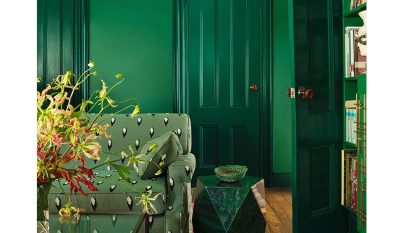 Green living room with matching walls, printed couch, stone table, glass coffee table, and bookshelv Green living room with matching walls, printed couch, stone table, glass coffee table, and bookshelv
