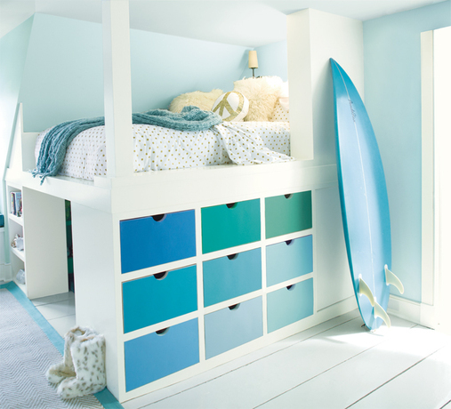 A kid's room with light blue-painted walls features a multi-hued bureau and surfboard. A kid's room with light blue-painted walls features a multi-hued bureau and surfboard.