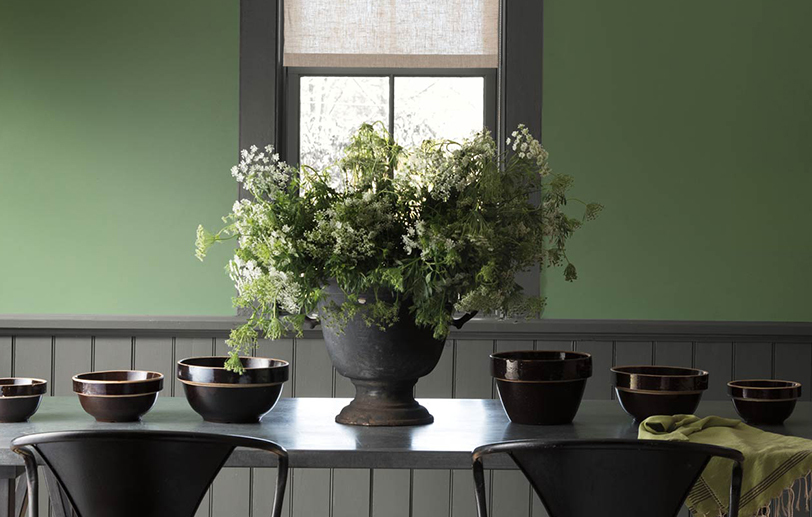 Green painted walls lighten this dining room with dark gray trim, wainscoting and table.