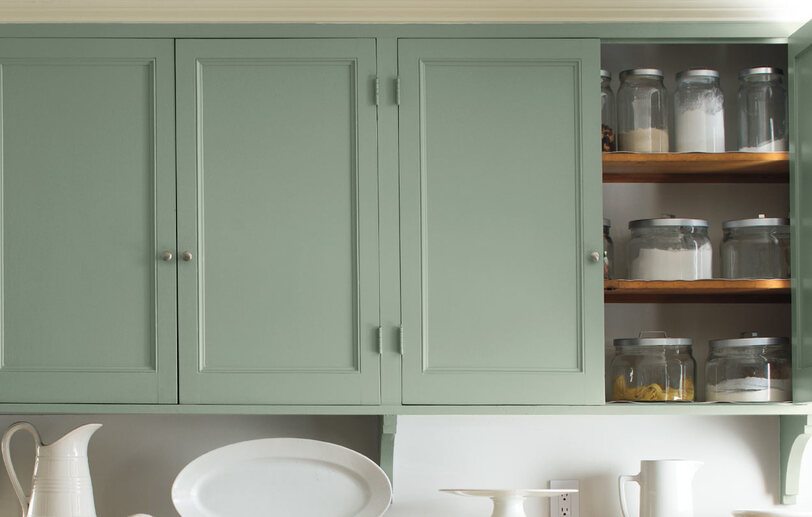 Light green cabinets add a soft glow as a backdrop to a dining table. Light green cabinets add a soft glow as a backdrop to a dining table.