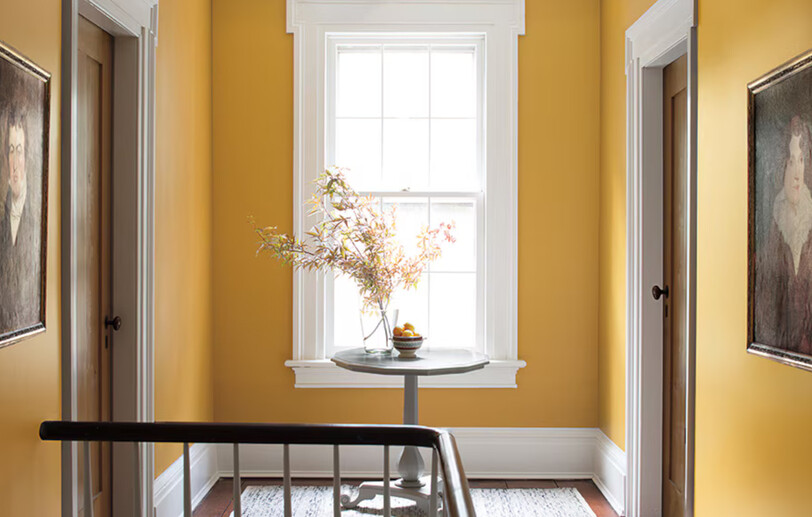 Yellow-painted hallway with wooden table and flowers, two doors, a window, and white-painted trim. Yellow-painted hallway with wooden table and flowers, two doors, a window, and white-painted trim.